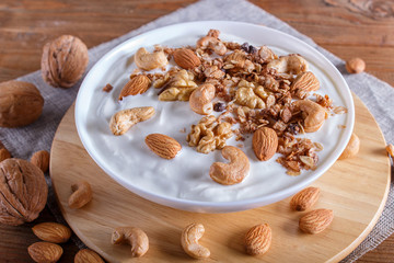 White plate with greek yogurt, granola, almond, cashew, walnuts  on brown wooden background.