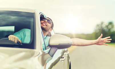 road trip, transport, travel and people concept - happy smiling man in sunglasses driving car and...