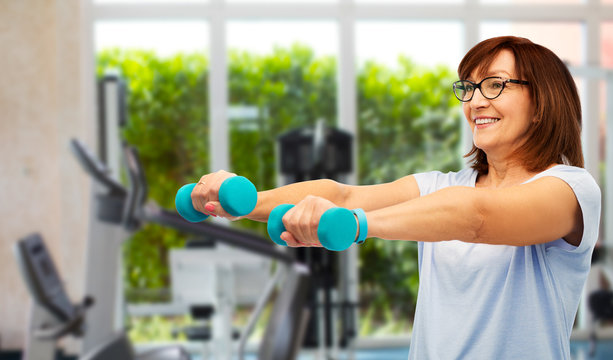 sport, healthy lifestyle and old people concept - smiling senior woman with dumbbells and fitness tracker exercising over gym background