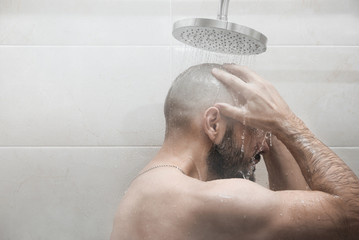A man washes in the shower. Side view.