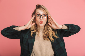 Portrait of excited blond woman 30s wearing jacket and eyeglasses expressing surprise on camera