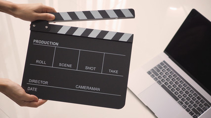 Hand is holding Black Movie slate or clapperboard and laptop use in video production ,film, cinema...