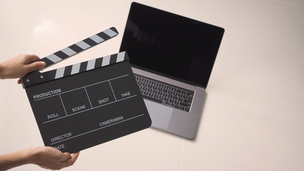 Fototapeta na wymiar Hand is holding Black Movie slate or clapperboard and laptop use in video production ,film, cinema industry on white background.