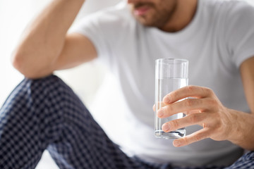 people, health and hydration concept - close up of unhealthy man suffering from hangover with glass...