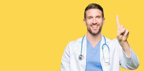 Handsome doctor man wearing medical uniform over isolated background showing and pointing up with finger number one while smiling confident and happy.