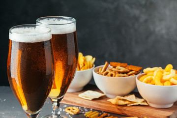 Glass of lager beer with snack bowls on dark stone background