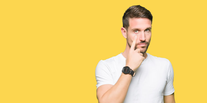 Handsome man wearing casual white t-shirt Pointing to the eye watching you gesture, suspicious expression