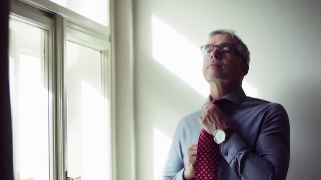 Mature businessman on a business trip standing in a hotel room, getting dressed.