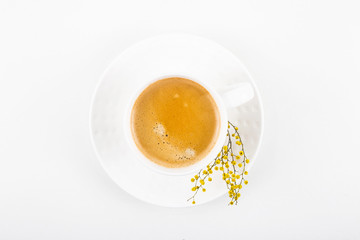 White cup of coffee on a white table with yellow mimosa flowers. Minimalism. Top view, flat lay