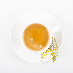 White cup of coffee on a white table with yellow mimosa flowers. Minimalism. Top view, flat lay