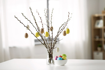 holidays and object concept - pussy willow branches decorated by easter eggs in vase on table