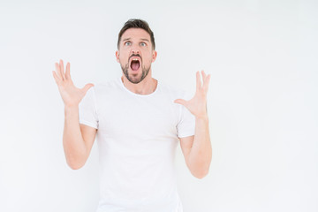 Fototapeta premium Young handsome man wearing casual white t-shirt over isolated background crazy and mad shouting and yelling with aggressive expression and arms raised. Frustration concept.