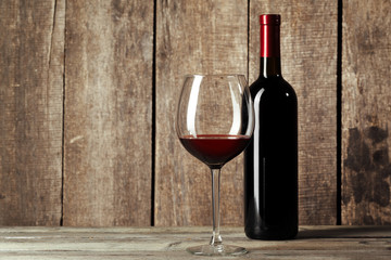 Glass and bottle with delicious red wine on table against wooden background