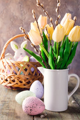 Yellow tulips in a vase and easter colorful eggs on a wooden table. Gift and Easter eggs.