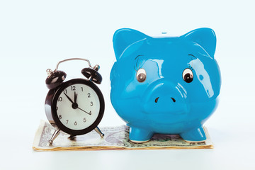 Piggy bank with clock on the heap of money.