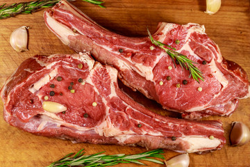Raw fresh beef rib eye steak on bone with spices, garlic and rosemary on wooden table. Top view