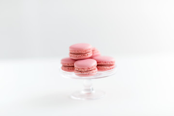 sweets, pastry and food concept - pink macarons on glass confectionery stand over white background