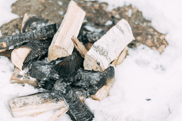 Stack of birch wood in the snow. Extinguished fire and coals on the boards.