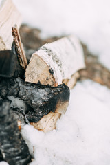 Stack of birch wood in the snow. Extinguished fire and coals on the boards.