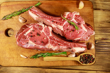 Raw fresh beef rib eye steak on bone with spices, garlic and rosemary on wooden table. Top view