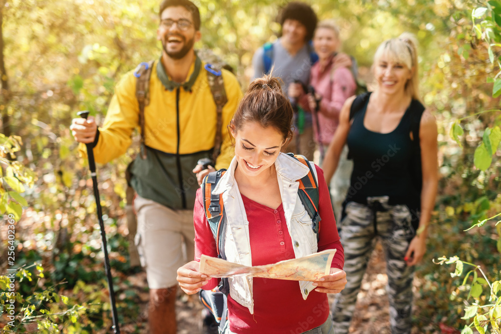 Wall mural Smiling beautiful brunette holding map and leading the rest of hikers through woods in autumn.