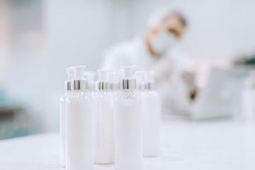 Close up of liquid soaps in bottles on the desk in lab. In background blurred chemist using laptop.