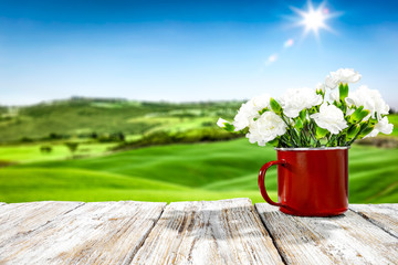 Fresh spring flowers in red mug on wooden white table and spring landscape 