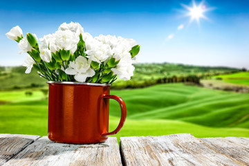 Fresh spring flowers in red mug on wooden white table and spring landscape 
