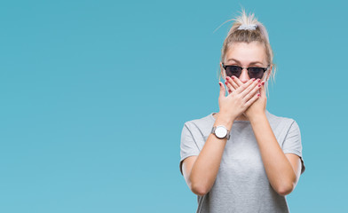 Fototapeta premium Young blonde woman wearing sunglasses over isolated background shocked covering mouth with hands for mistake. Secret concept.