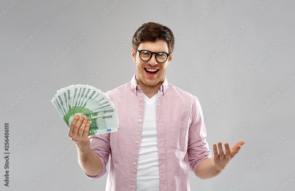 Wall mural money, finance, business and people concept - happy young man in glasses with fan of one hundred euro bank notes over grey background