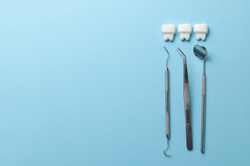 Healthy white teeth on blue background and dentist tools mirror, hook. Copy space for text.