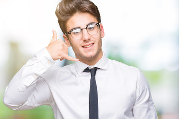 Young business man wearing glasses over isolated background smiling doing phone gesture with hand and fingers like talking on the telephone. Communicating concepts.