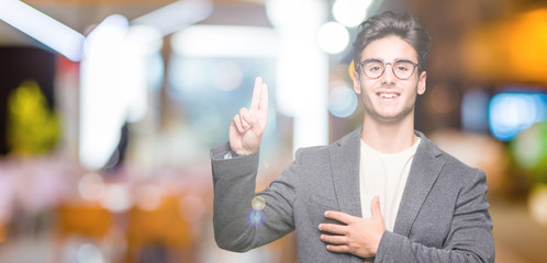 Young business man wearing glasses over isolated background Swearing with hand on chest and...