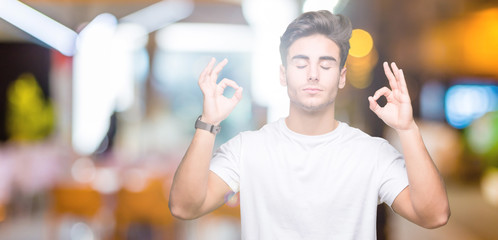 Fototapeta na wymiar Young handsome man wearing white t-shirt over isolated background relax and smiling with eyes closed doing meditation gesture with fingers. Yoga concept.