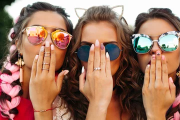  Close-up van drie jonge meisjes die een creatieve zonnebril dragen met ontworpen manicure, twee dames dekken de mond en een verbergend gezicht met de handen. Happy vrienden poseren en plezier samen. © Вячеслав Косько