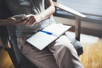 Young woman in casual clothes sitting at table in home and writing in notebook. Freelancer working...