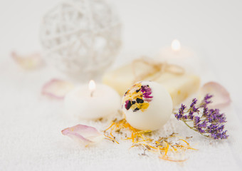 Obraz na płótnie Canvas Beautiful set with selective focus on white creamy moisturizing small bath ball bomb with dry flower blossom petals, spa candles burning and dry flower pieces scattered around. Instagram filter.