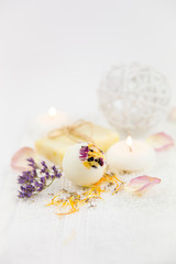 Obraz na płótnie Canvas Beautiful set with selective focus on white creamy moisturizing small bath ball bomb with dry flower blossom petals, spa candles burning and dry flower pieces scattered on white clean soft towel.