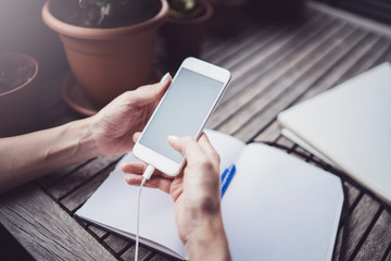Young business woman sitting at table in caffee terrace and taking notes in notebook.On table is smartphone and paper documents. Student learning online or blogger concept