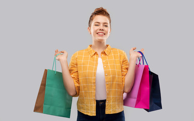 sale, outlet and people concept - smiling red haired teenage girl in checkered shirt with shopping bags over grey background
