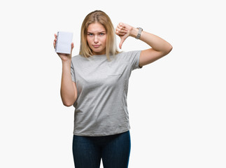Young caucasian woman holding blank notebook over isolated background with angry face, negative sign showing dislike with thumbs down, rejection concept