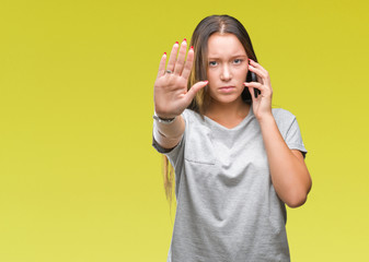 Young beautiful caucasian woman talking on smartphone over isolated background with open hand doing stop sign with serious and confident expression, defense gesture