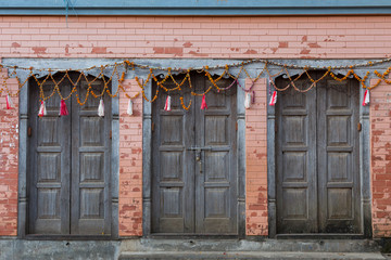 Three beautiful old blue-grey wooden doors decorated with garlands and set in pale pink brick in historic town of Bandipur, Nepal