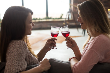 Two best friends girls having fun drink wine, smiling and gossip, joyful sisters celebrating birthday party, elegant stylish clothes