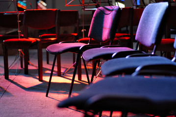 Empty places for orchestra on stage. The chairs are lit by red and blue light floodlights.