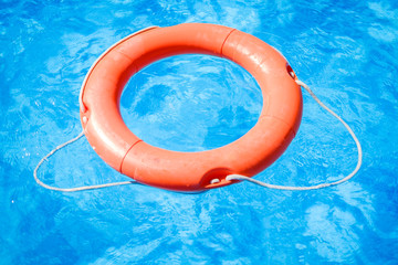 Closeup view of the swimming pool with blue water and a red ring life buoy floating on it during a sunny summer day
