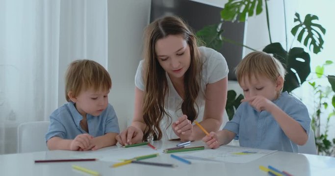 Mom helps two sons of 2 and 4 years old to do preschool homework to draw a picture with pencils