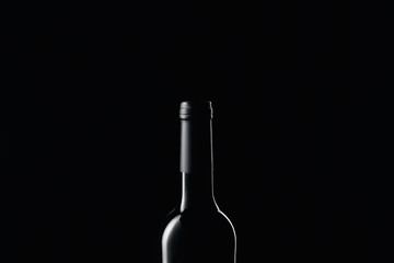Glass wine bottle in darkness isolated on black