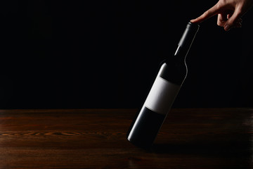 Partial view of woman touching wine bottle on wooden surface isolated on black