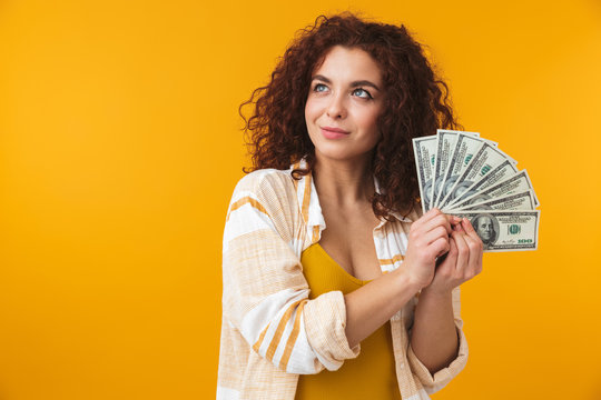 Beautiful emotional young curly girl posing isolated over yellow wall background holding money.